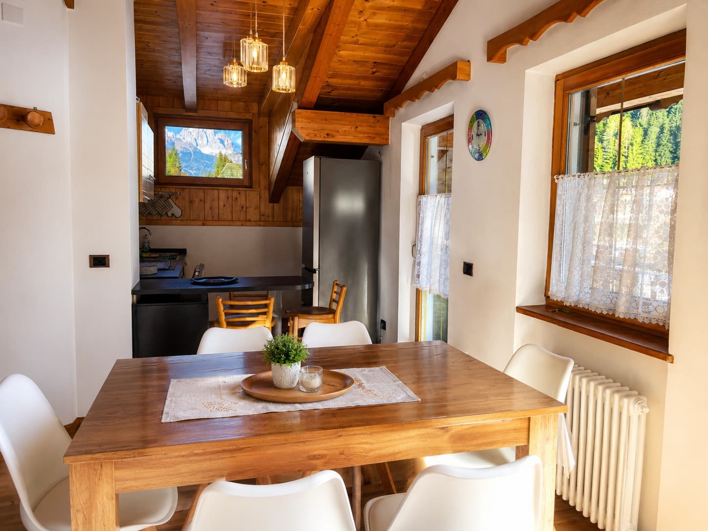 Zona pranzo con tavolo in legno, travi a vista e lampade di design: luce naturale e vista panoramica sulle Dolomiti