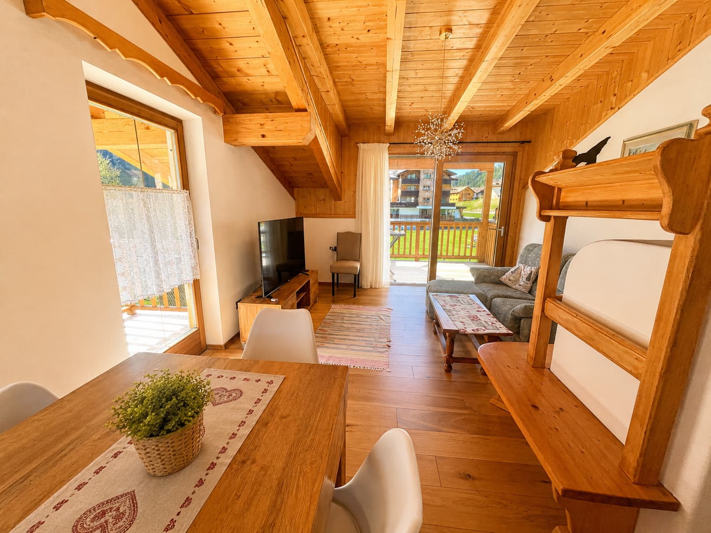 Vista completa del soggiorno: spazio ampio con travi massicce, divani, TV, lampadario decorativo e balcone panoramico